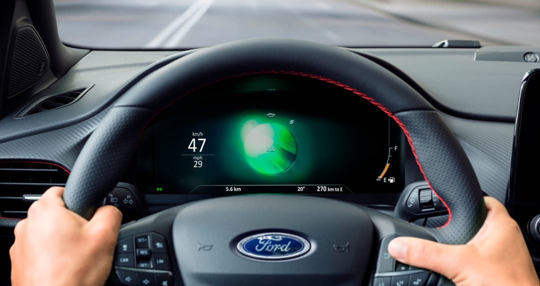 Tableau de bord du nouveau Ford Puma avec écran numérique affichant l'autonomie en mode hybride et les mains du conducteur sur le volant