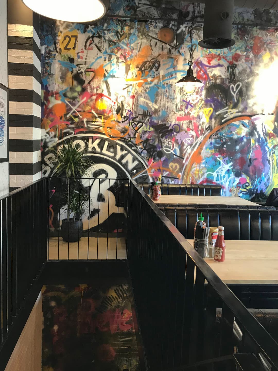 Intérieur de Black Tap Genève avec murs couverts de street art coloré, mobilier noir, luminaires suspendus et plantes vertes