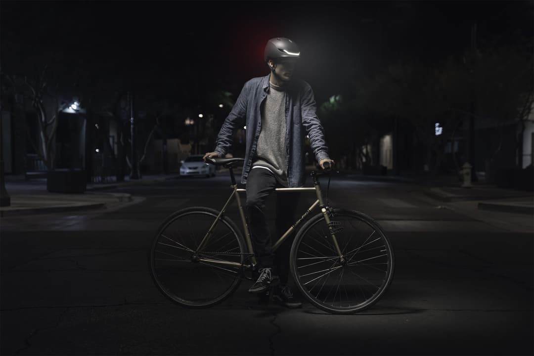 Cycliste de nuit portant un casque Lumos avec LED intégrées éclairées, immobilisé avec son vélo en ville
