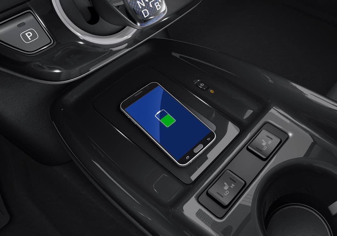 Intérieur de la Toyota Prius Plug-in Hybrid avec plateau de charge sans fil affichant un téléphone en cours de recharge, éléments décorés en noir élégant