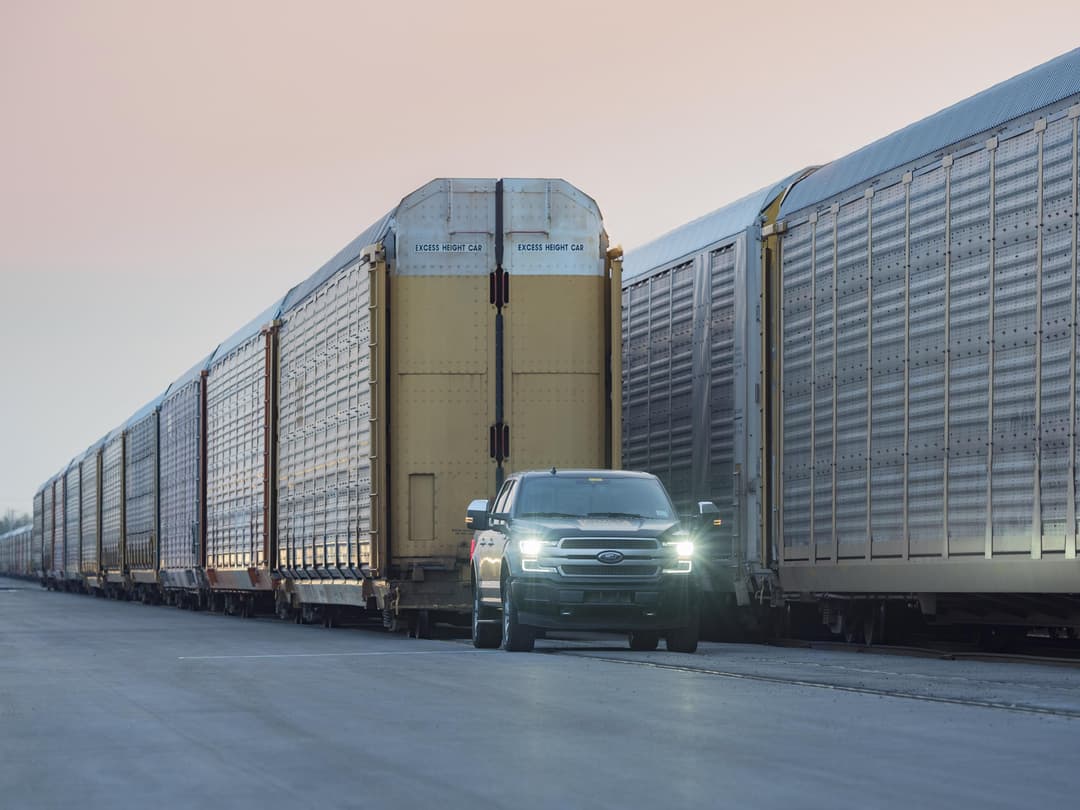 Ford F-150 électrique blanc tirant une remorque de transport de véhicules chargée de 42 pick-ups