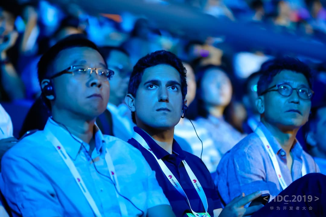 Trois hommes regardent vers l'écran lors de la conférence HDC 2019 de Huawei, éclairés par la lumière bleue de la présentation