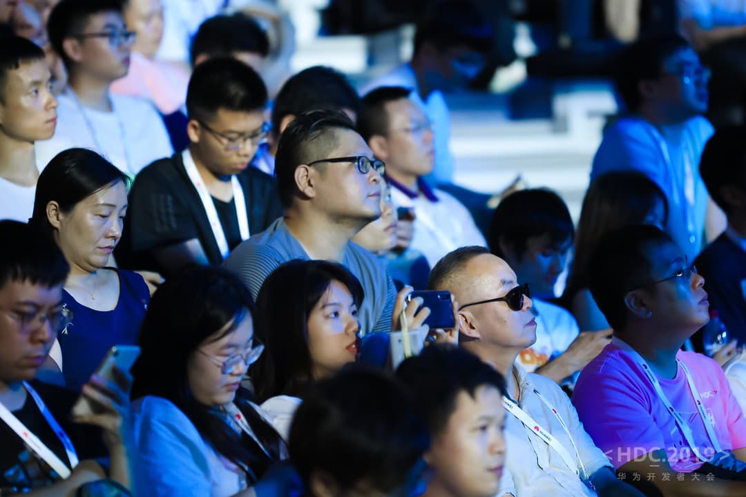 Audience de développeurs et partenaires Huawei écoutant une présentation lors d'une conférence, certains tenant des smartphones