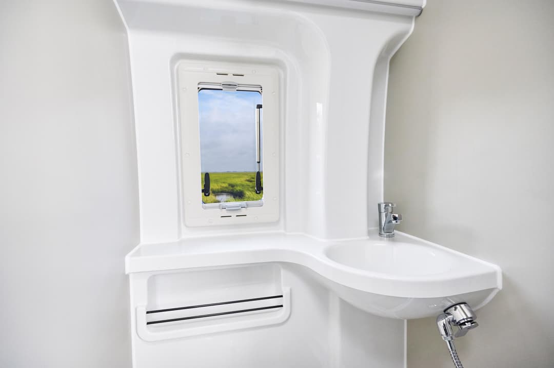 Intérieur blanc minimaliste du Ford Big Nugget avec fenêtre ouverte sur paysage verdoyant, lavabo et rangements