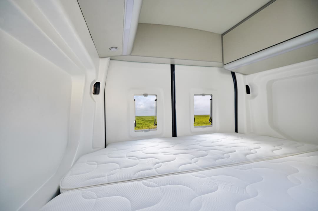 Intérieur du concept Ford Big Nugget avec lit blanc spacieux et deux fenêtres donnant sur un paysage verdoyant