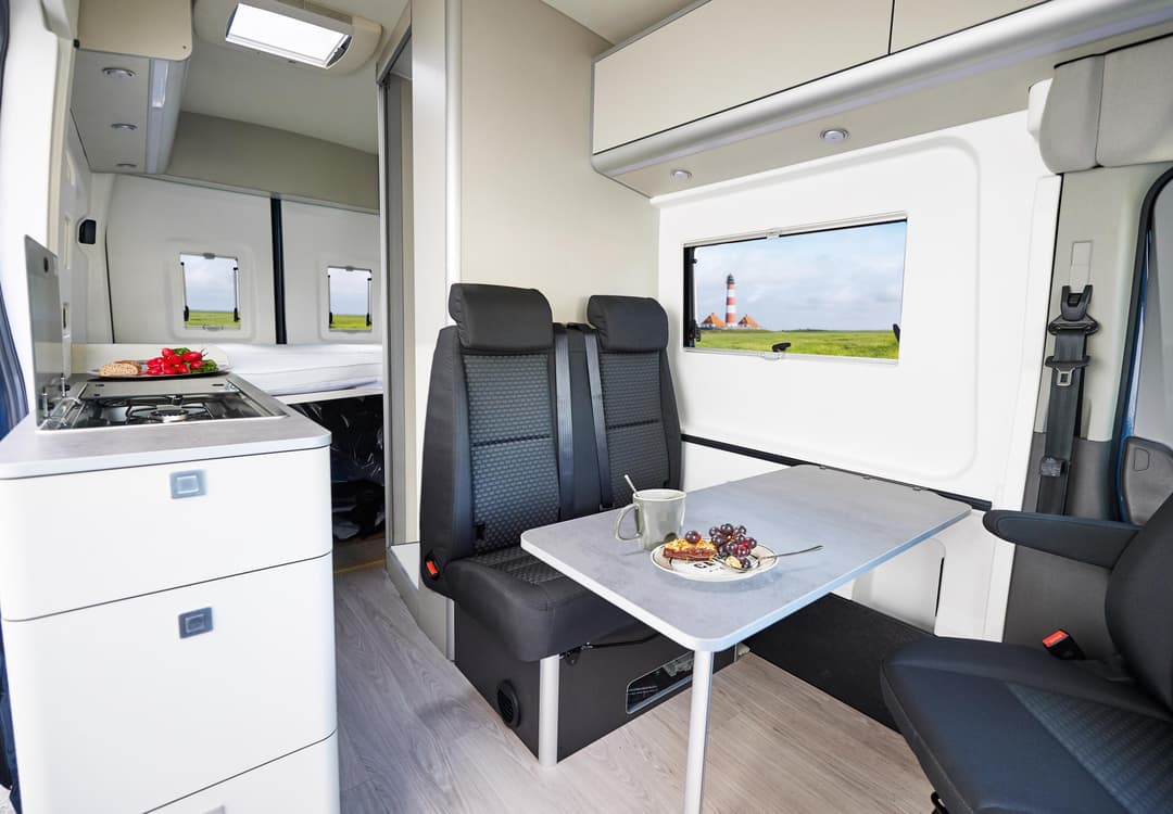 Intérieur du camping-car Ford Big Nugget avec coin cuisine blanc, table de repas et sièges noirs