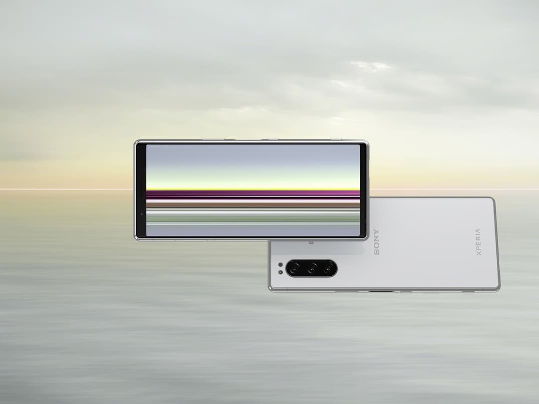 Sony Xperia 5 blanc avec écran allumé affichant un paysage côtier, vue de face et de dos montrant le module photo triple