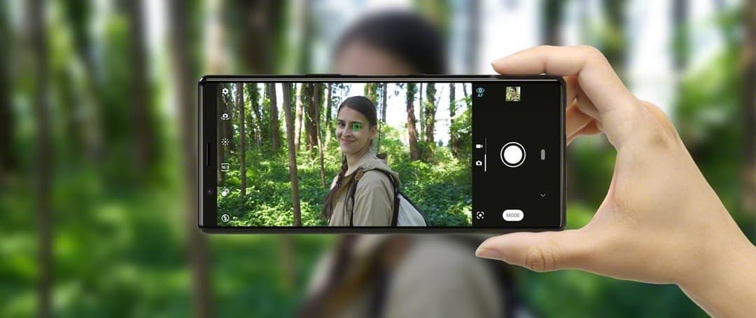 Sony Xperia 5 tenu en main en mode paysage, affichant l'écran de prise de vue d'une femme dans une forêt
