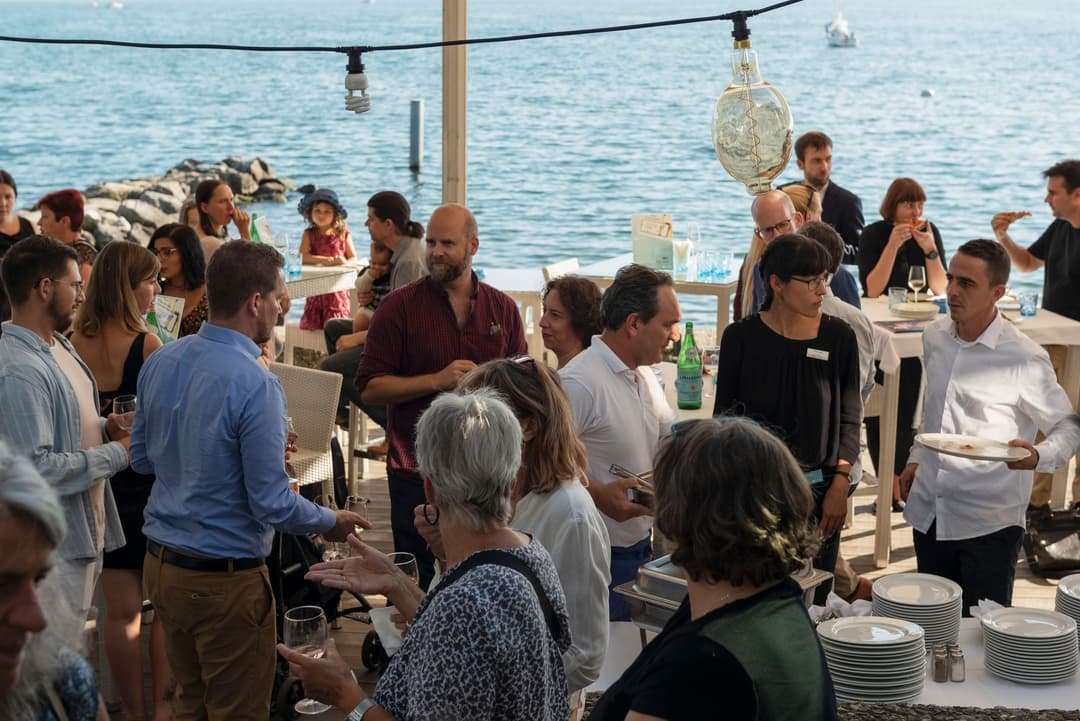 Groupe de personnes lors d'un événement en terrasse au bord de la mer, discutant et dégustant des boissons