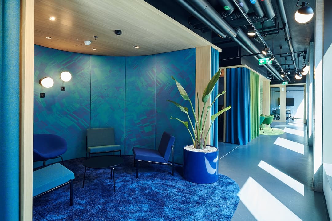 Espace de détente aux murs bleus avec fauteuils, plante verte et luminaires, siège social de Google Suisse