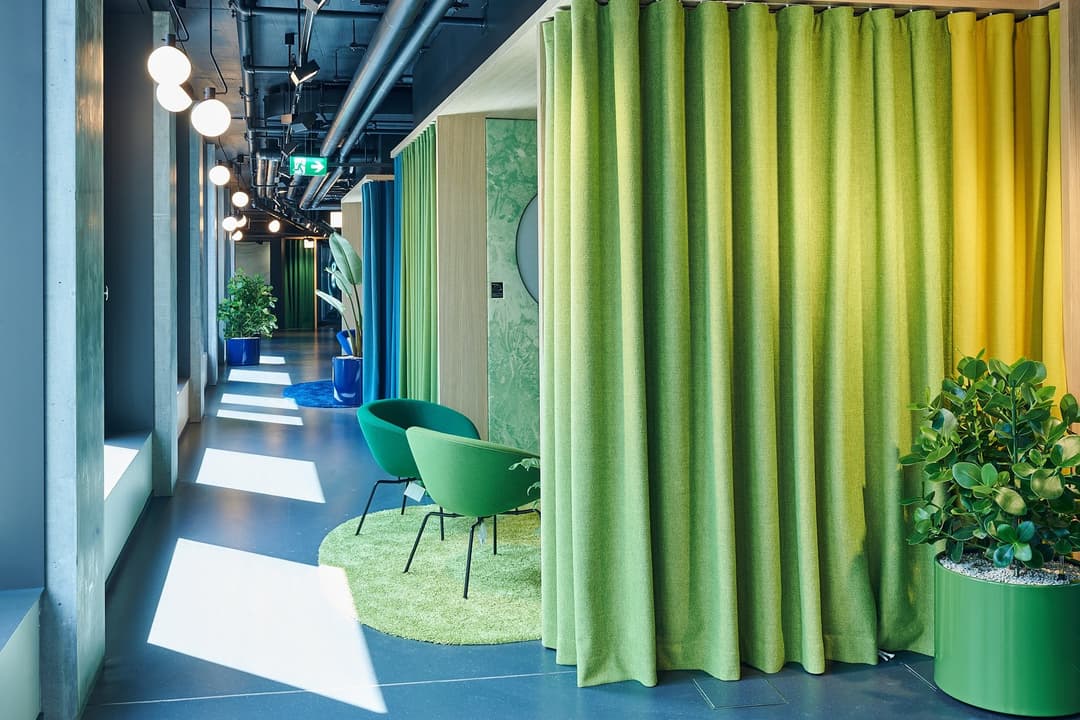Couloir moderne d'un bureau Google avec rideaux verts, chaises design, végétation, lumière naturelle et signalétique, symbolisant un espace de travail innovant