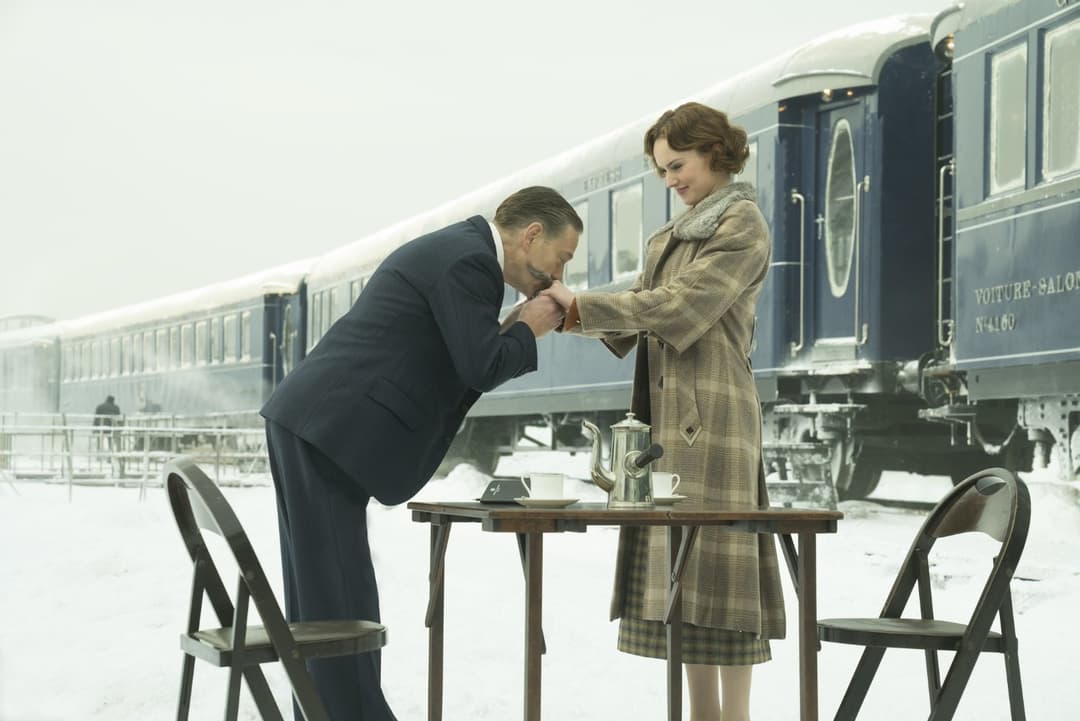 Deux personnages devant l'Orient-Express, l'homme en costume sombre baise la main de la femme vêtue d'un manteau à carreaux