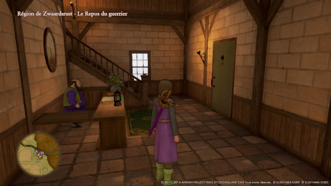 Intérieur d'une auberge en pierre du jeu Dragon Quest XI S, avec un personnage en robe violette au centre et un PNJ assis à gauche