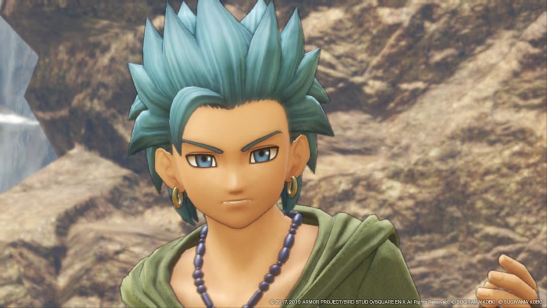 Personnage de Dragon Quest XI S aux cheveux bleu-vert pointus, portant une tunique verte, collier de perles, devant un décor rocheux