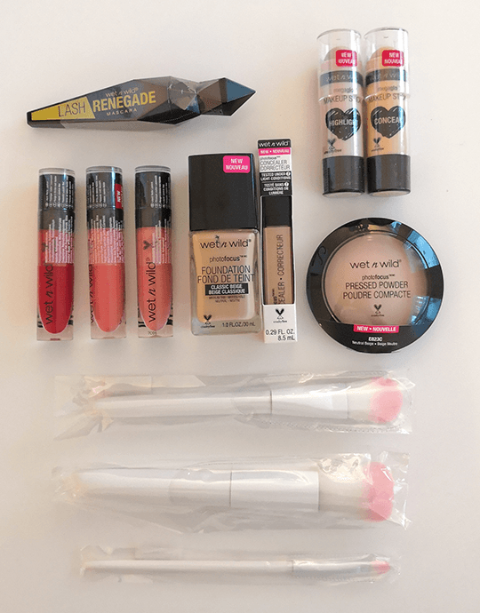 Coffret maquillage Wet n Wild composé de trois rouges à lèvres liquides roses, un eyeliner noir, une base de teint beige, une poudre compacte rose, deux baumes à lèvres et accessoires