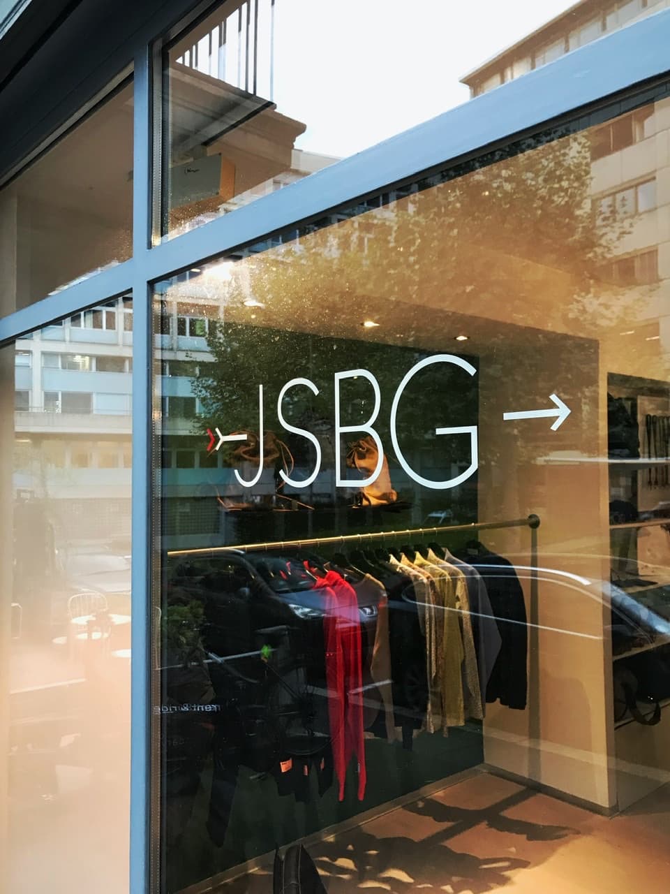 Devanture du JSBG Store avec enseigne lumineuse blanche sur vitrine, présentant vêtements et accessoires de créateurs suisses indépendants