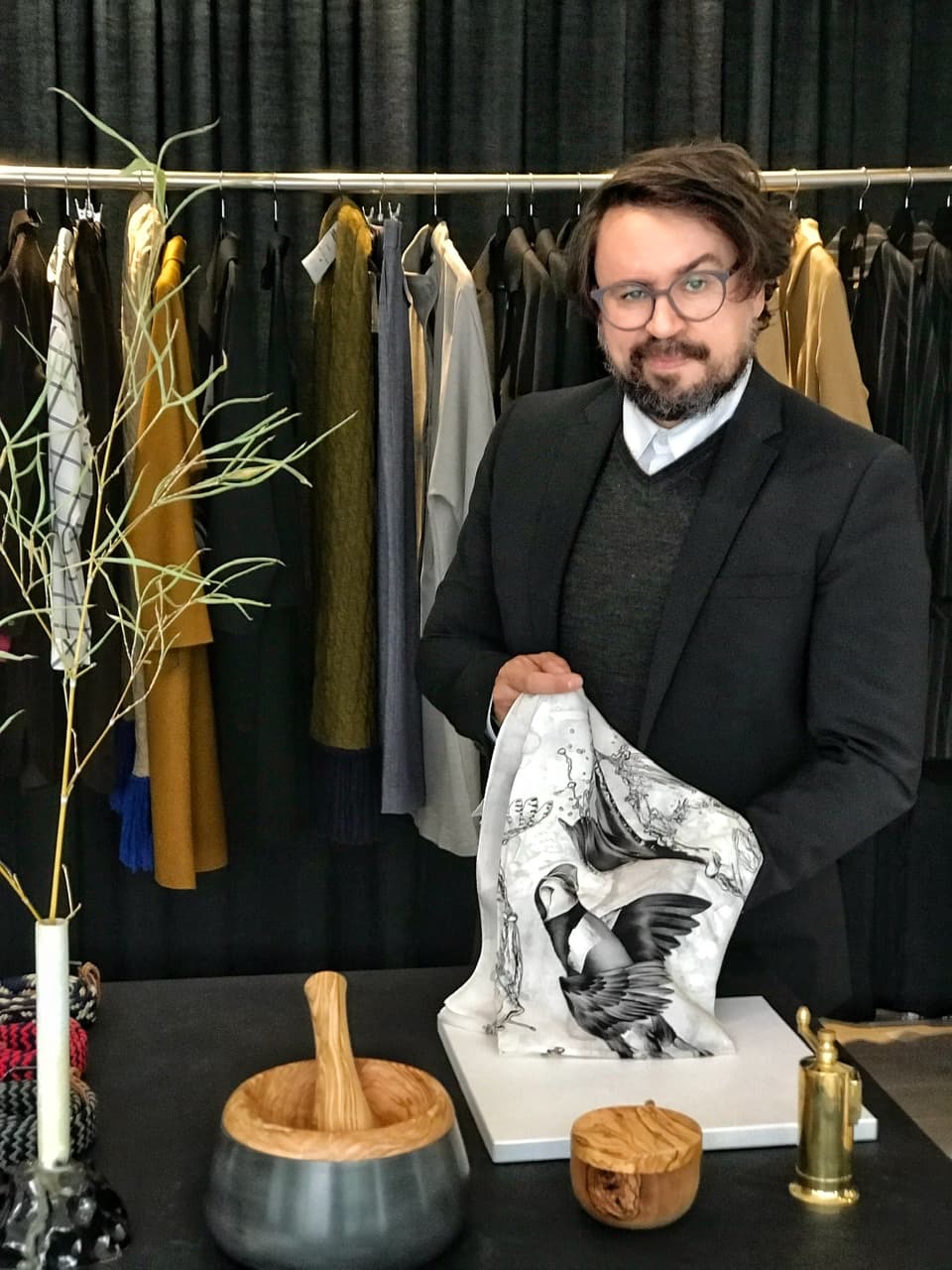 Jorge S. B. Guerreiro devant des vêtements de créateurs suisses indépendants exposés au JSBG Store, tenant une pièce textile blanche