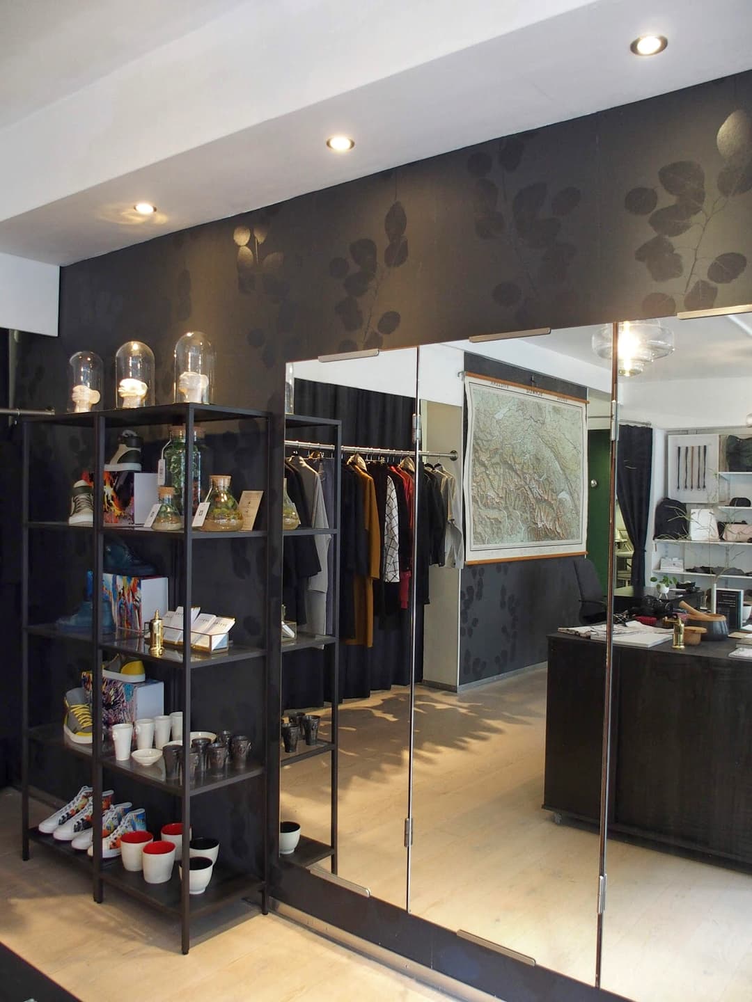 Intérieur du JSBG Store à Lausanne avec étagères noires exposant des créations suisses, vêtements sur cintres et murs gris ornés de motifs végétaux