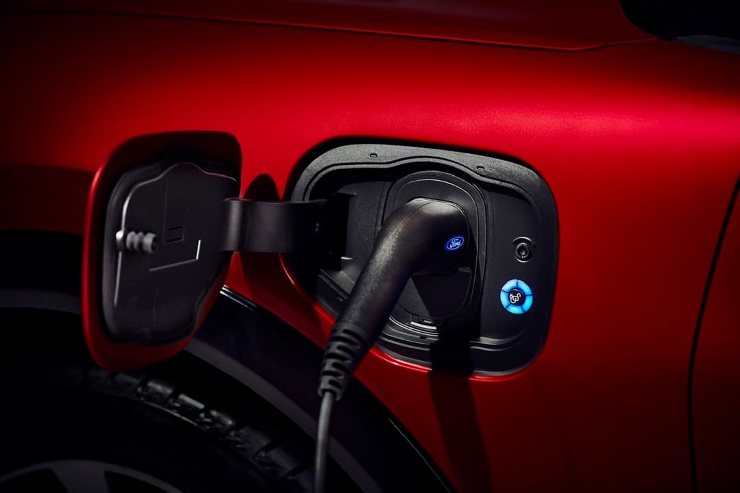 Prise de recharge de la Ford Mustang Mach-E électrique, câble branché sur le port noir avec logos Ford et batterie bleus, carrosserie rouge