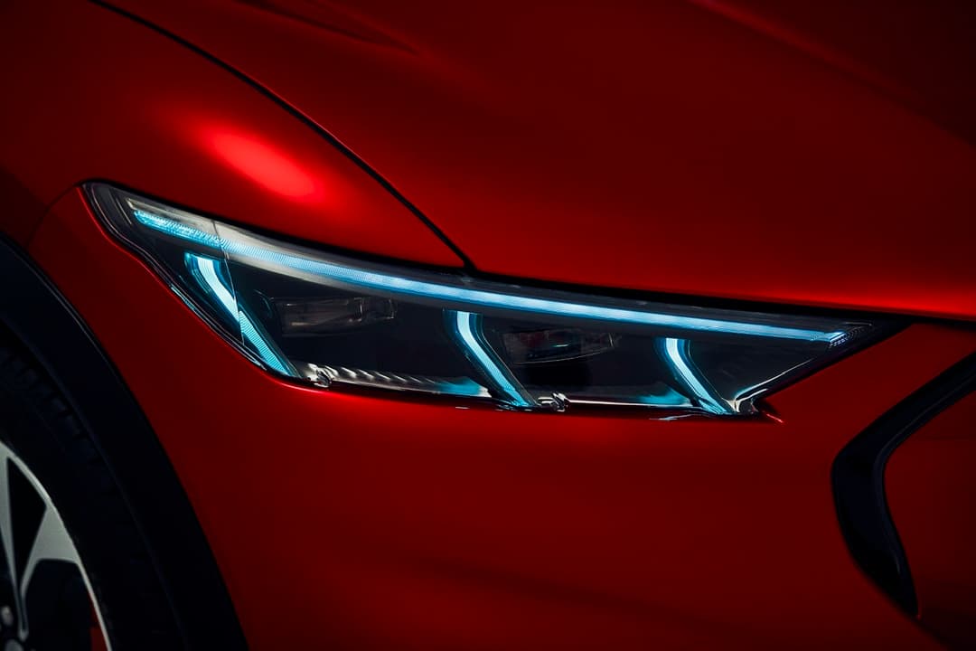 Détail du phare avant de la Ford Mustang Mach-E avec technologie LED bleue et blanche sur carrosserie rouge