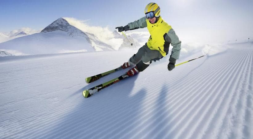 Skieur en tenue jaune et verte dévale une piste enneigée avec skis Scott Xplor'Air, montagne en arrière-plan