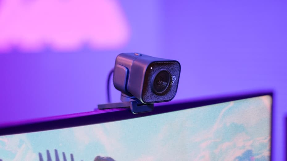 Caméra Logitech StreamCam noire fixée sur le cadre supérieur d'un écran, sur fond dégradé rose et violet