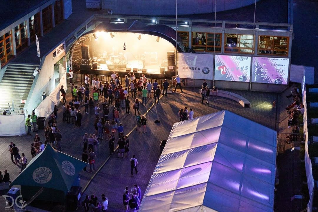 Aérienne du Baleinev Festival avec scène illuminée, structures gonflables bleues et violettes, et centaines de spectateurs sur l'esplanade