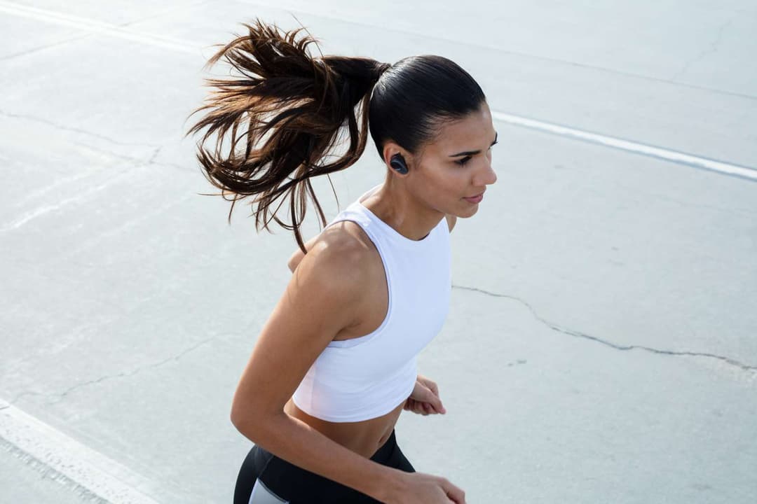 Femme en tenue de sport blanc et noir portant des écouteurs sans fil Sony WF-SP800 en train de courir en extérieur