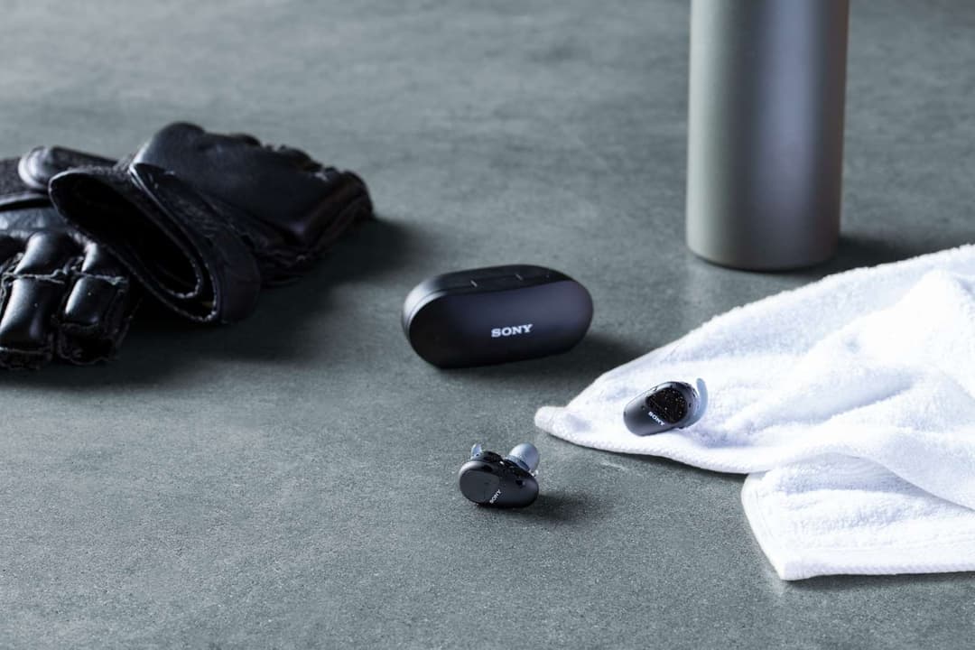 Écouteurs sans fil Sony WF-SP800 noirs avec boîtier de recharge, accompagnés d'une serviette et d'équipements de sport