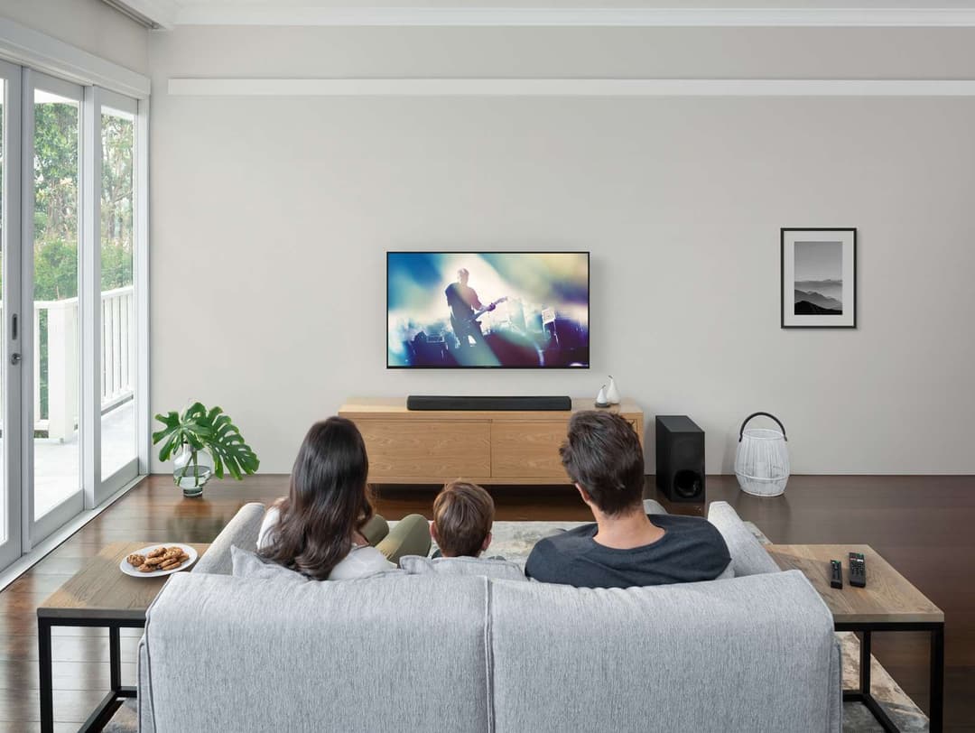 Famille regardant la télévision dans un salon, avec barre de son Sony noire sous l'écran et caisson de basses à côté