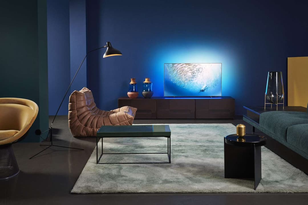 Téléviseur Philips OLED affichant un paysage marin, intégré dans un salon moderne aux tons bleus et noirs