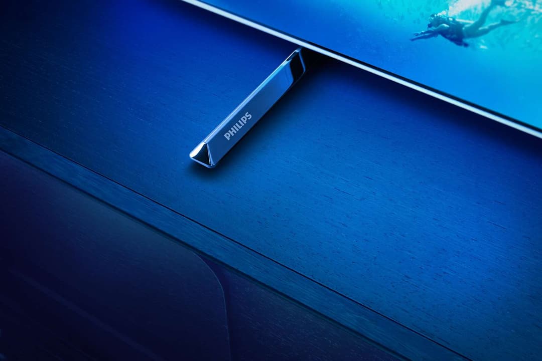 Télécommande premium Philips aux finitions chromées posée sur un téléviseur OLED bleu affichant une scène sous-marine
