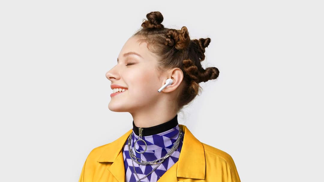 Jeune femme souriante portant des écouteurs blancs Huawei FreeBuds 3i et une veste jaune
