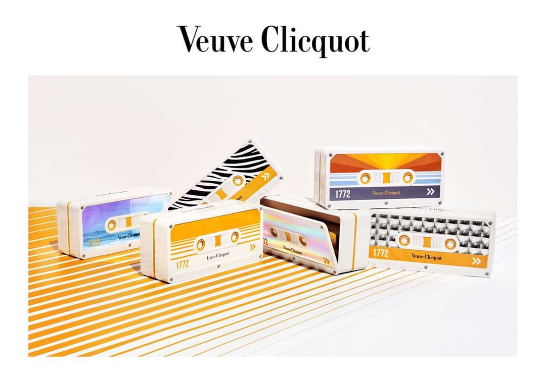 Cassettes audio de Veuve Clicquot aux designs rétro multicolores jaunes et bleus, avec logos de la maison, disposées sur un fond rayé