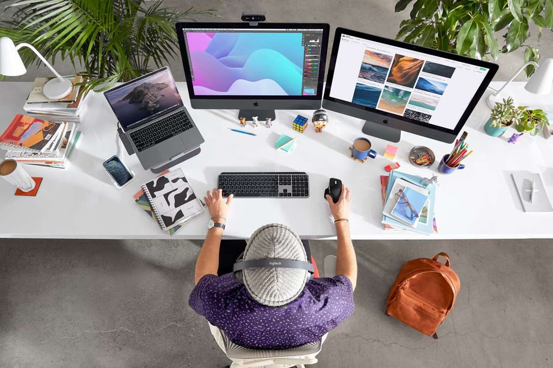 Espace de travail créatif avec clavier MX Keys gris, souris MX Master 3 gris, MacBook, deux écrans et accessoires de designer