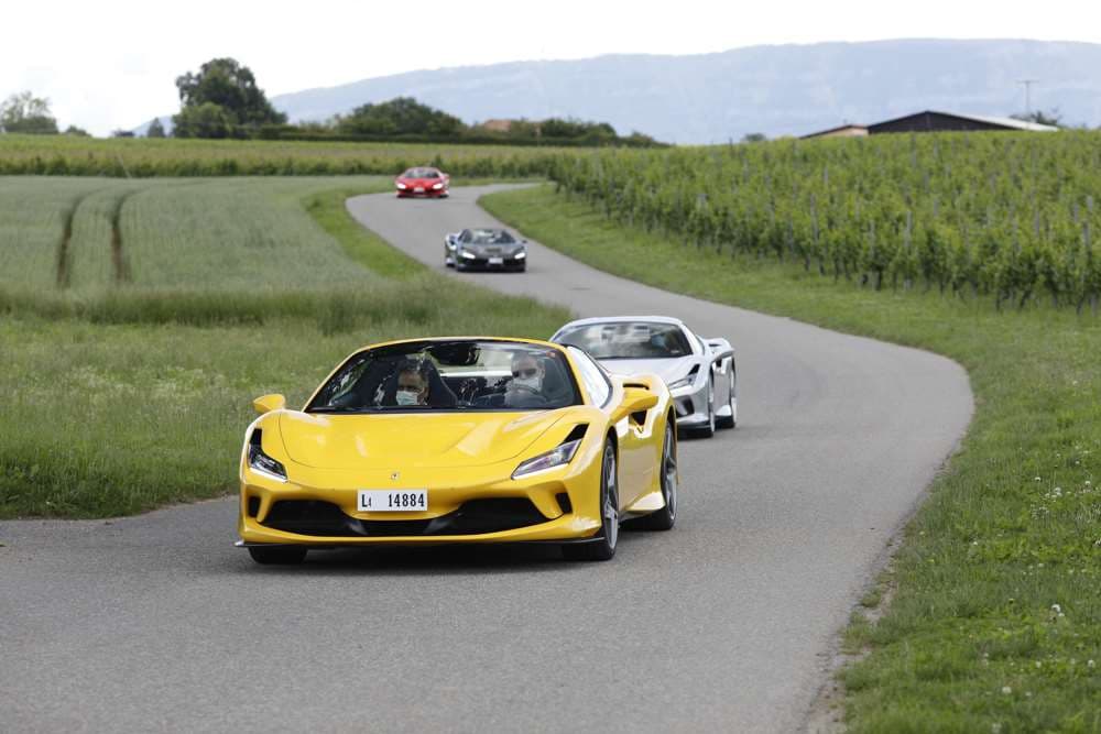 Quatre Ferrari roulent en convoi sur une route sinueuse à travers des vignes, dont une F8 Spider jaune en première position