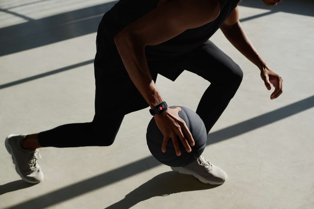 Sportif en tenue noire portant une OPPO Watch au poignet, tenant un ballon de basket en plein exercice
