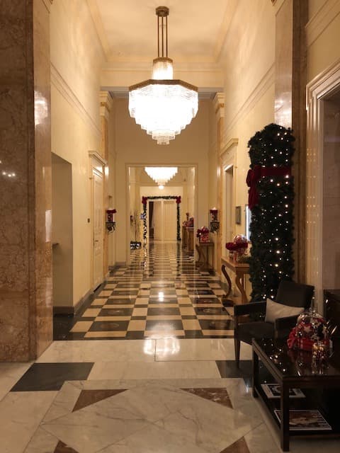 Couloir majestueux du Beau-Rivage Palace avec lustre en cristal, sol en marbre géométrique noir et blanc, et sapin décoré de boules rouges