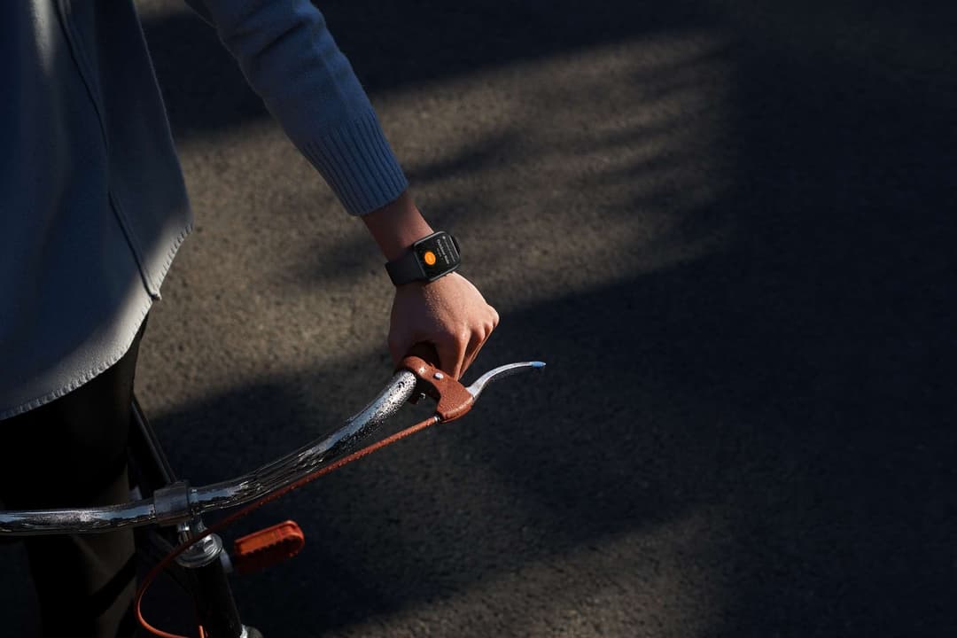 Montre OPPO Watch au poignet d'une personne tenant le guidon d'un vélo, affichage orange visible