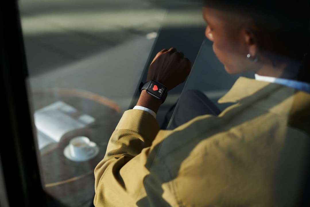 OPPO Watch au poignet d'une personne vêtue d'un pull jaune, affichant un cœur rouge sur son écran AMOLED