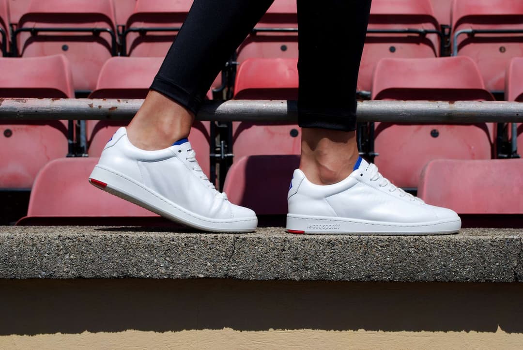 Paire de sneakers blanches Le Coq Sportif aux couleurs du FC Lausanne-Sport portée dans les gradins roses du stade