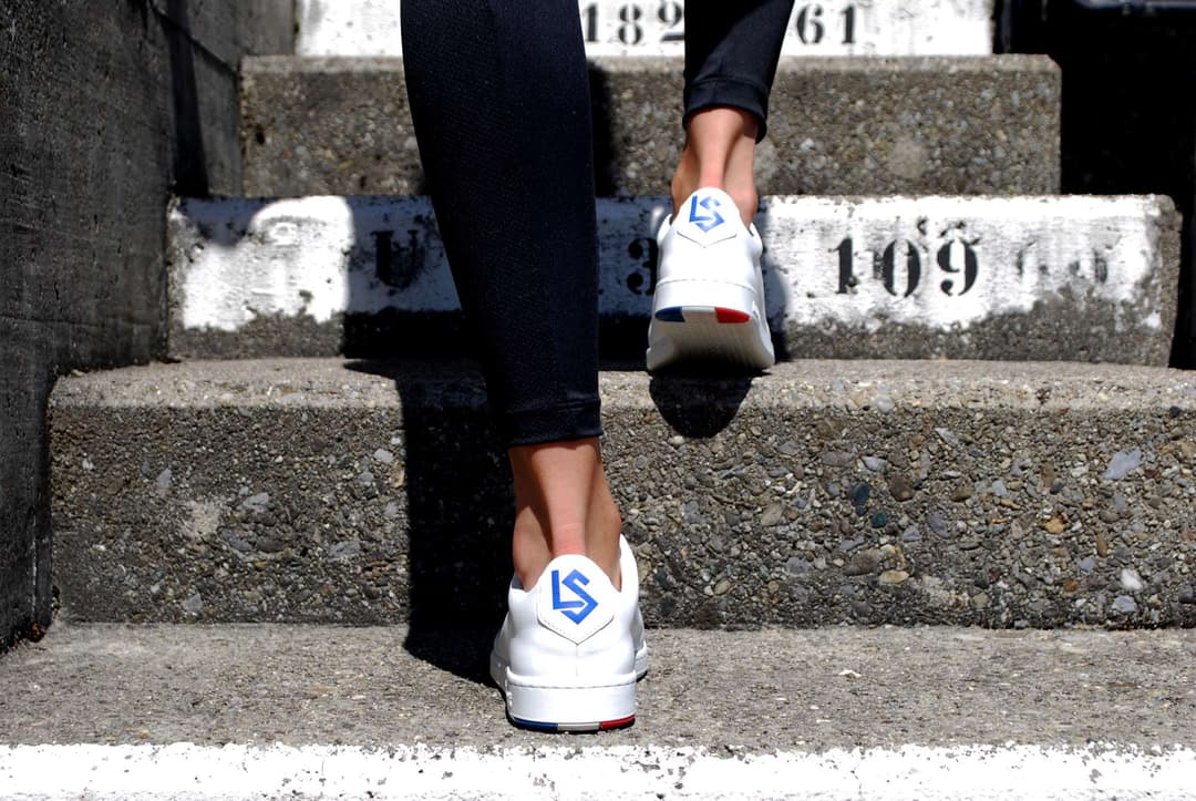 Chaussures Blazon Le Coq Sportif X FC Lausanne-Sport blanches avec écusson bleu aux initiales LS, portées sur des marches numérotées