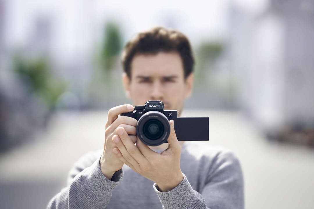 Homme tenant un appareil photo Sony Alpha 7S III noir avec écran articulé, photographiant en extérieur