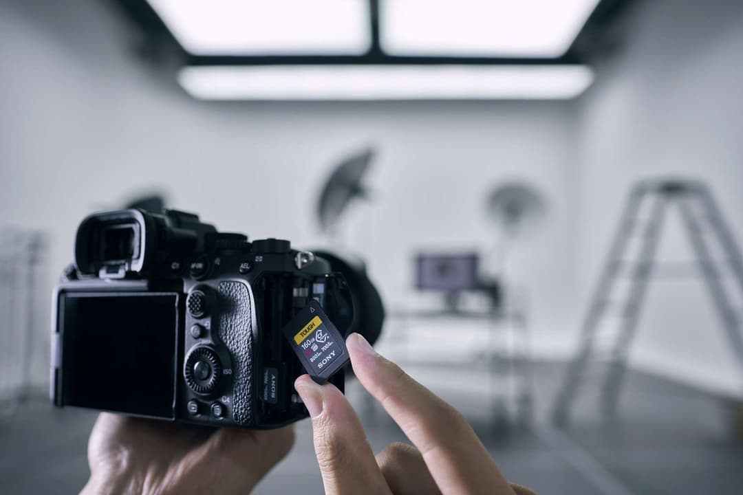 Sony Alpha 7S III noir tenu en main avec une carte mémoire CFexpress Type A jaune, dans un studio blanc équipé