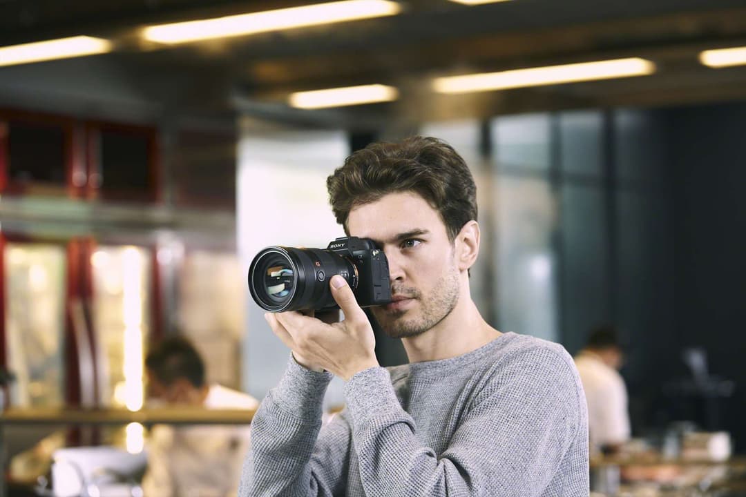 Photographe tenant un Sony Alpha 7S III, appareil photo mirrorless noir, en position de prise de vue dans un intérieur moderne
