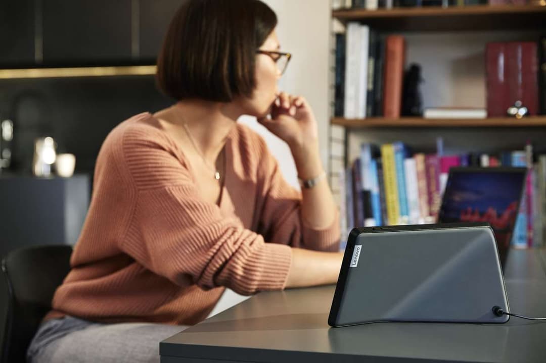 Lenovo ThinkSmart View, tablette noire avec écran tactile, posée sur un bureau face à une femme en pull terracotta