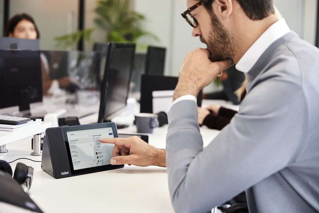 Homme en chemise bleue utilisant un Lenovo ThinkSmart View lors d'une réunion en open space avec collègues