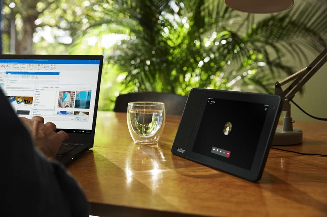 Lenovo ThinkSmart View affichant un appel vidéo sur son écran tactile, posé sur un bureau à côté d'un ordinateur portable