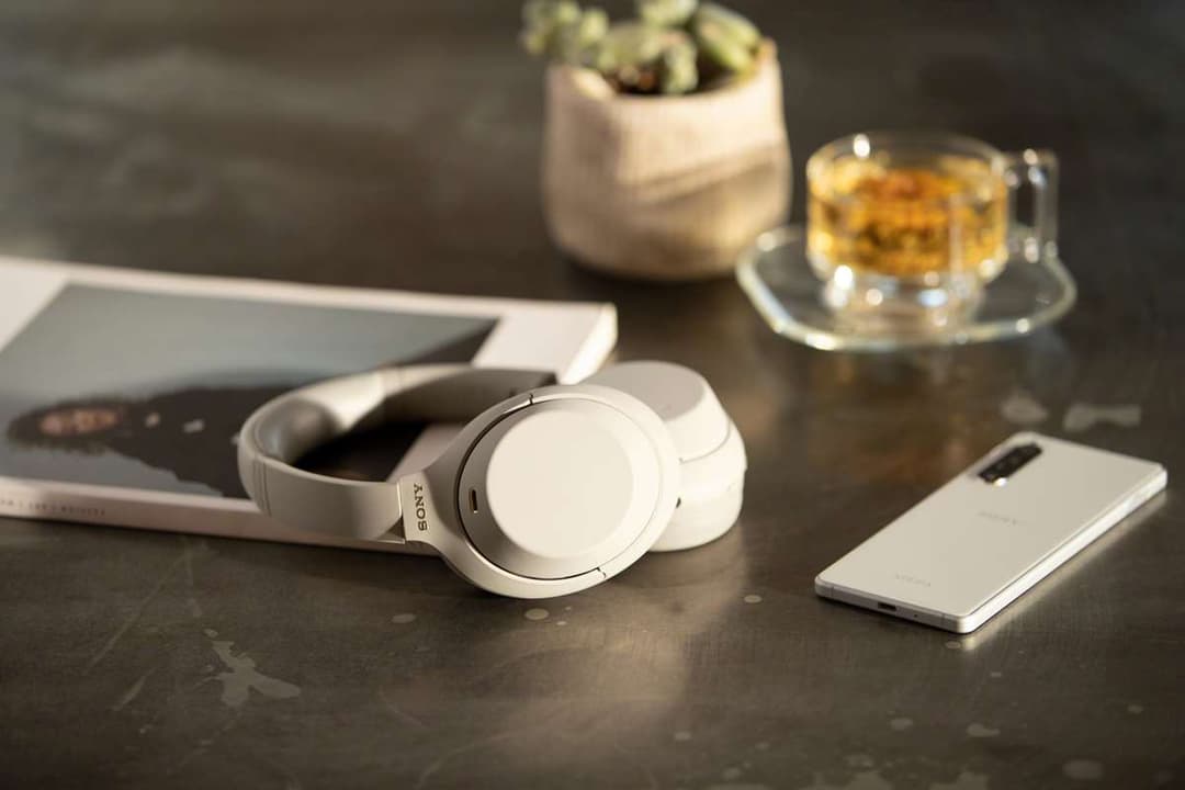 Casque Sony WH-1000XM4 blanc sur un bureau gris, à côté d'un smartphone, avec tablette et verre de whisky en arrière-plan
