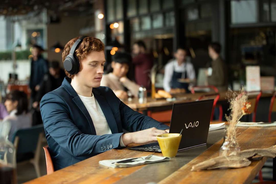 Homme portant un casque Sony WH-1000XM4 noir travaillant sur un ordinateur portable dans un café
